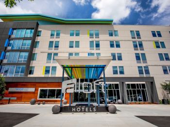 This image shows the exterior of an Aloft Hotel featuring a modern design, with large windows and a colorful canopy over the entrance.