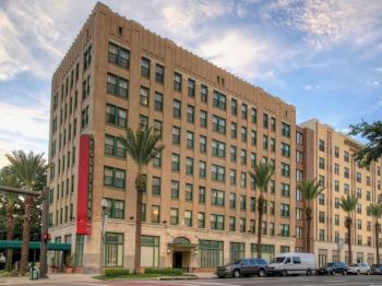 This image shows a multi-story building with multiple windows, palm trees, parked vehicles, and a blue sky with clouds in the background.