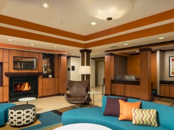 A modern lobby features colorful seating, a fireplace, geometric decor, and a front desk in the background.