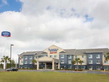 This image features a Fairfield Inn & Suites by Marriott hotel with a blue and beige exterior, situated in a landscaped area with palm trees.