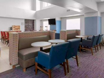 A modern lounge area with cushioned seating, tables, and a TV on the wall. The design includes blue and green chairs and a red dining area.