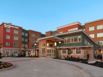The image shows the exterior of a Residence Inn by Marriott hotel, featuring a modern design with plants and a well-maintained driveway ending the sentence.